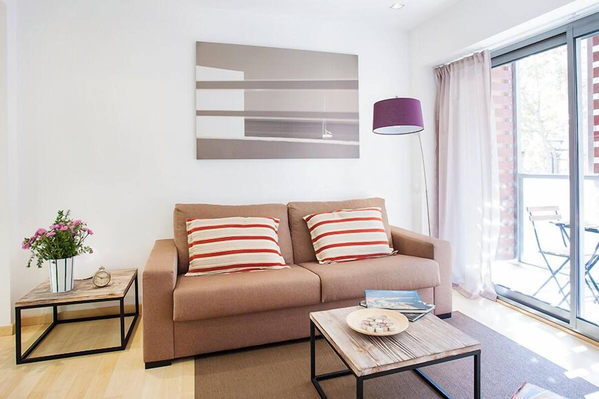 Una sala moderna con un sofá, una mesa de centro, una mesita auxiliar con una planta y un ventanal con cortinas.