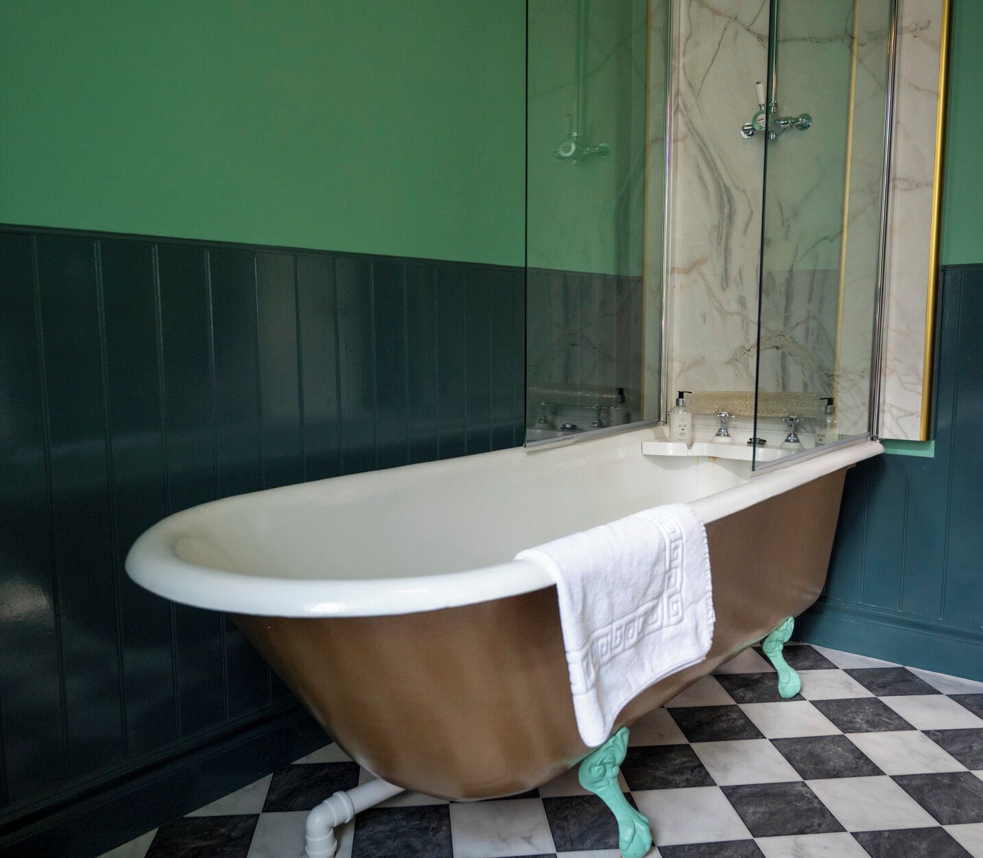 Een badkamer met een vrijstaand bad, een spiegel en een zwart-wit betegelde vloer.