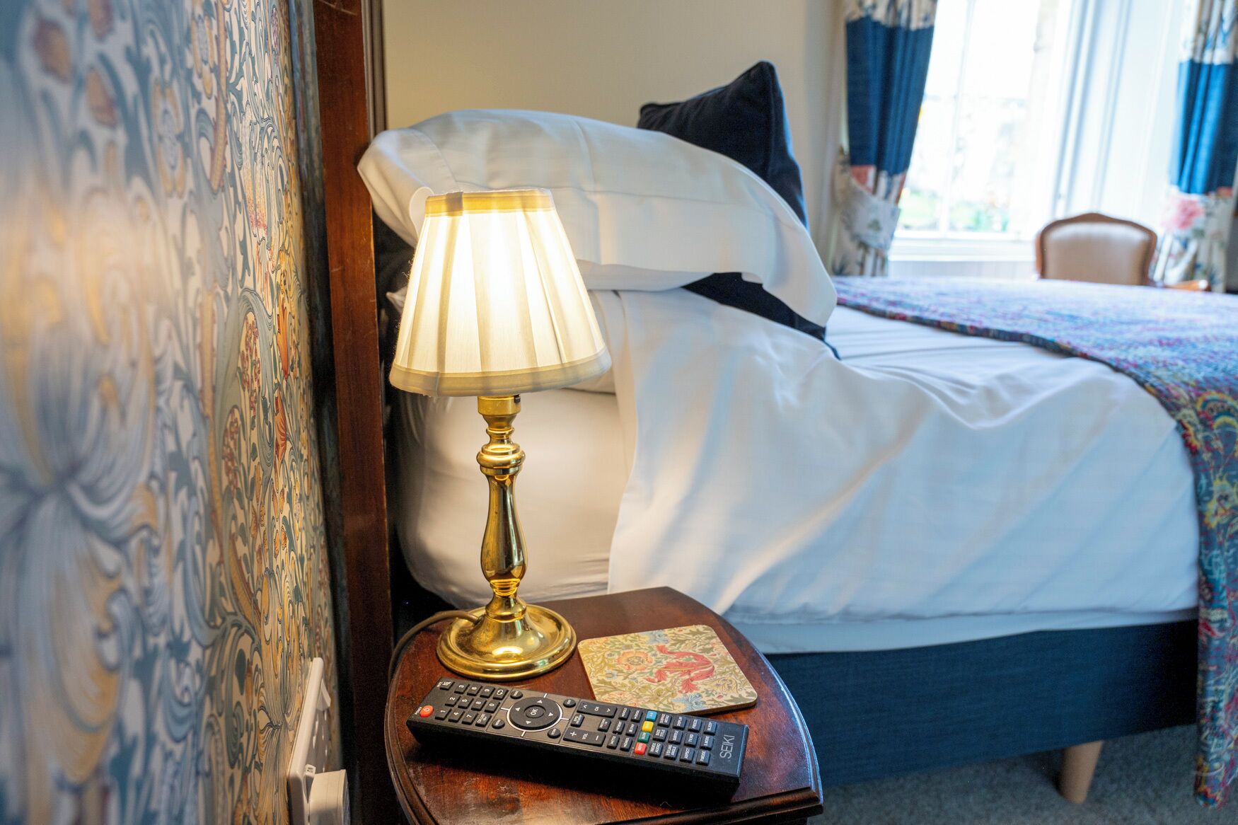 A hotel room with a bed, a bedside lamp, a remote control, and a decorative pillow.