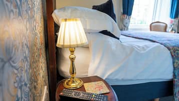 A hotel room with a bed, a bedside lamp, a remote control, and a decorative pillow.