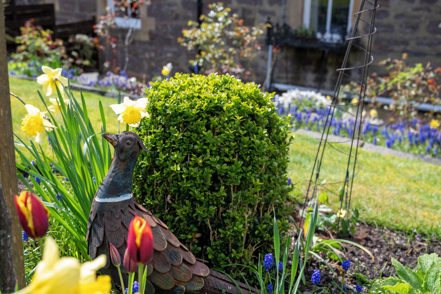 Un jardin agrémenté d’une sculpture d’oiseau, de fleurs et d’un arbuste taillé avec soin.