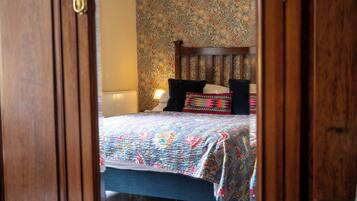 A bedroom with a patterned wallpaper, a wooden headboard, and a bed with a colorful quilt.