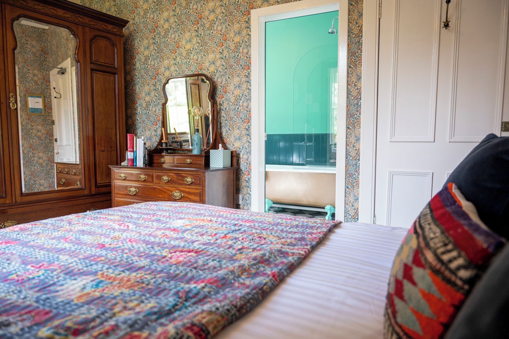 A bedroom with a bed, dresser, mirror, and a view of a bathroom.