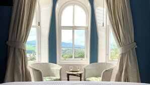 A bedroom with a large bed, two white chairs, a small table with glasses, and a window with curtains. - Leven House (Crieff)