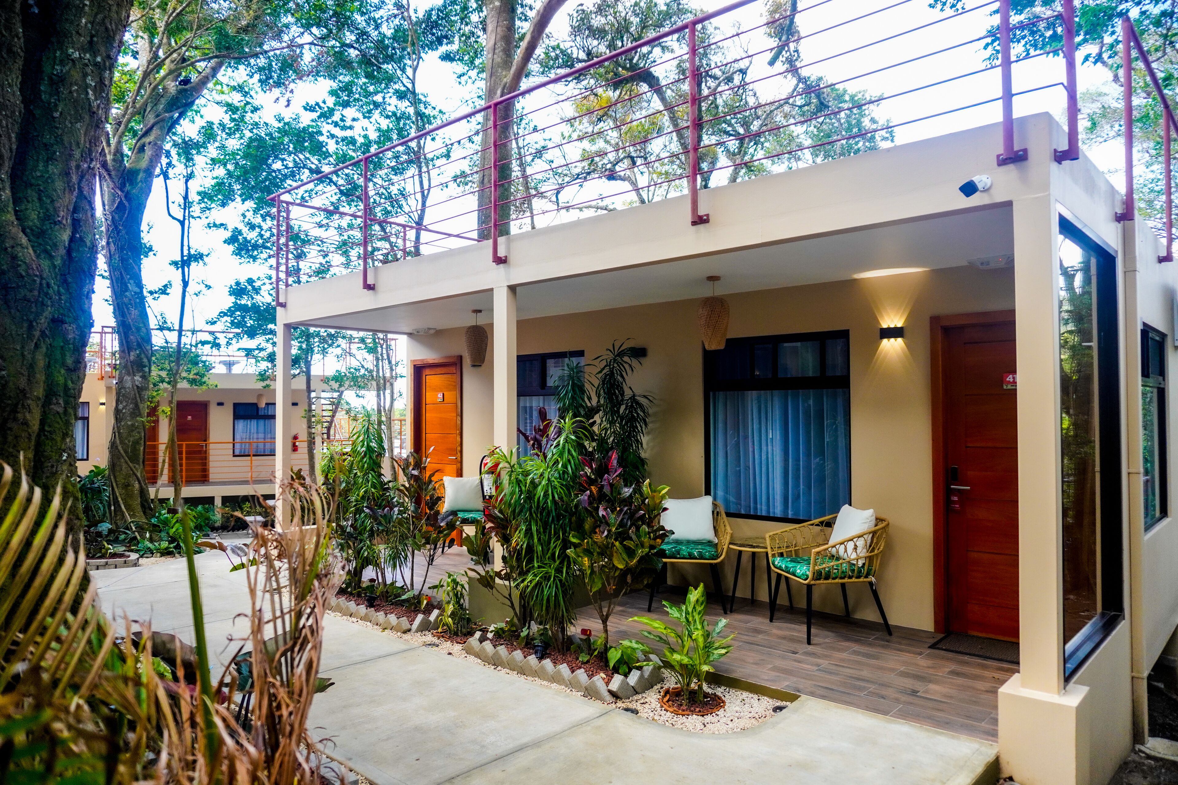 A two-story building with a covered outdoor seating area, surrounded by lush greenery and trees.