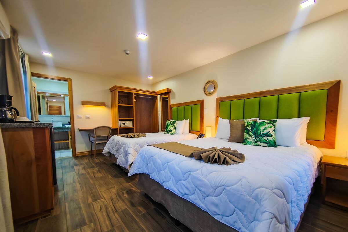 A hotel room with two beds, a wooden wardrobe, a desk with a coffee maker, and a mirror.