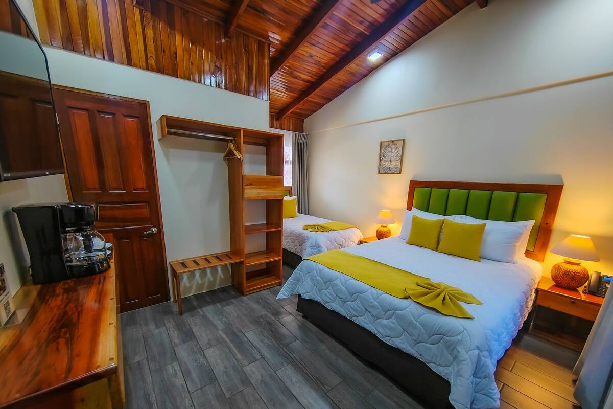 A hotel room with two beds, wooden flooring, a wooden wardrobe, a coffee machine, and a small shelf.