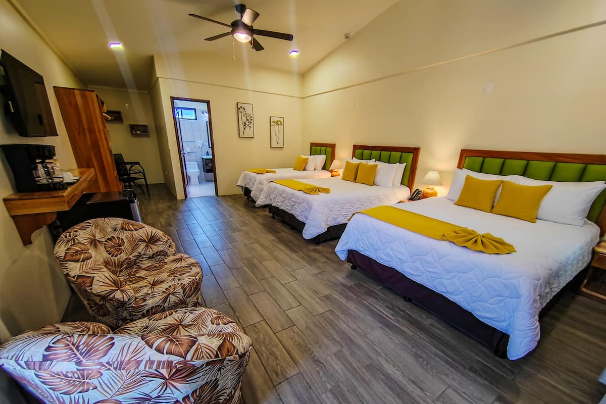 A hotel room with three beds, a desk, a chair, and a ceiling fan.