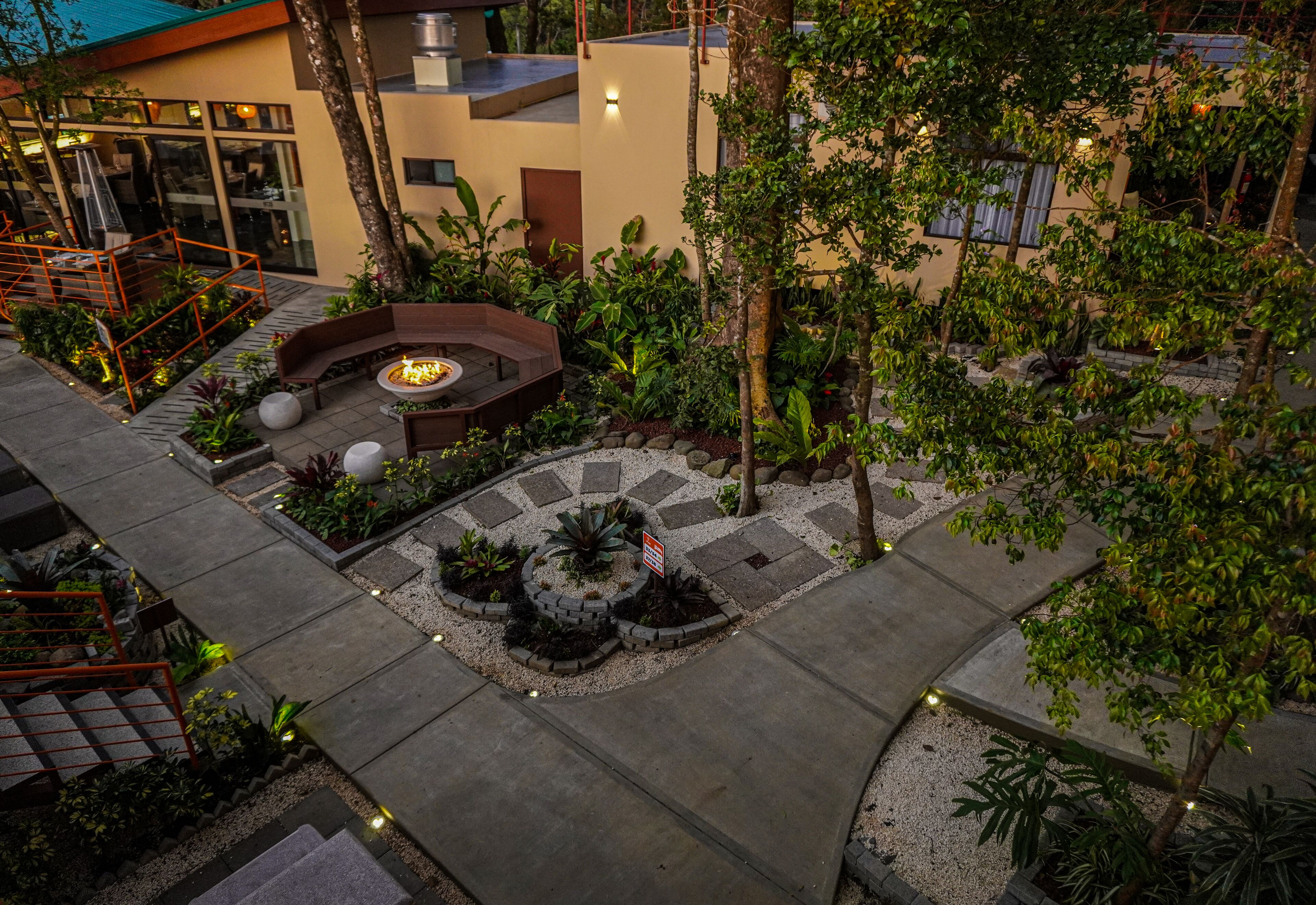 A modern outdoor patio with a fire pit, seating areas, and a variety of plants.