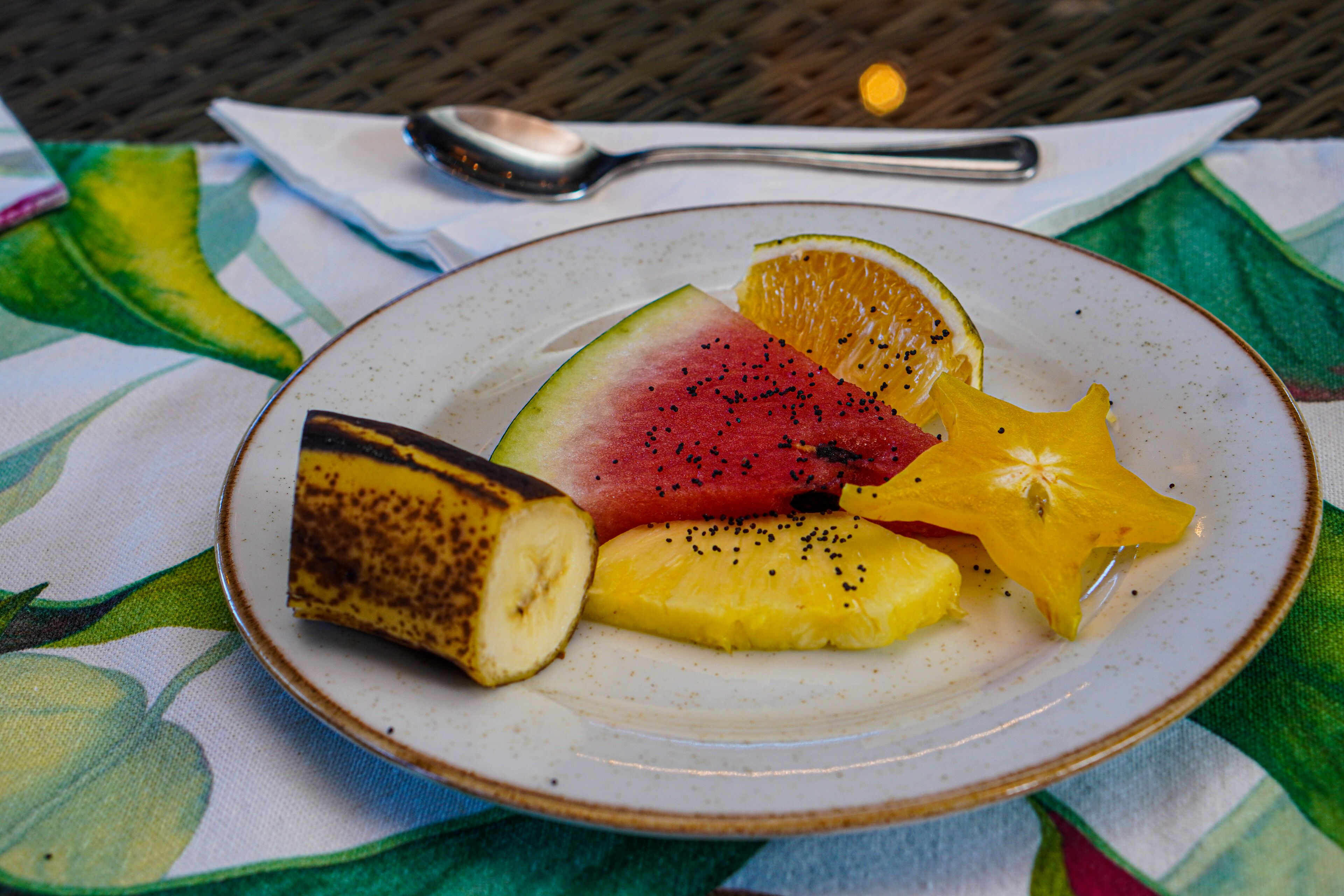 Un plato con sandía, piña, plátano y rodajas de naranja sobre un mantel.