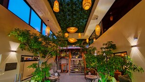 A hotel lobby with a central staircase, multiple seating areas, and indoor plants. - Sibu Boutique Hotel (Monteverde)