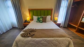 Habitación de hotel con una cama grande, cabecera verde, dos lámparas de noche, una mesita de noche de madera y un armario.