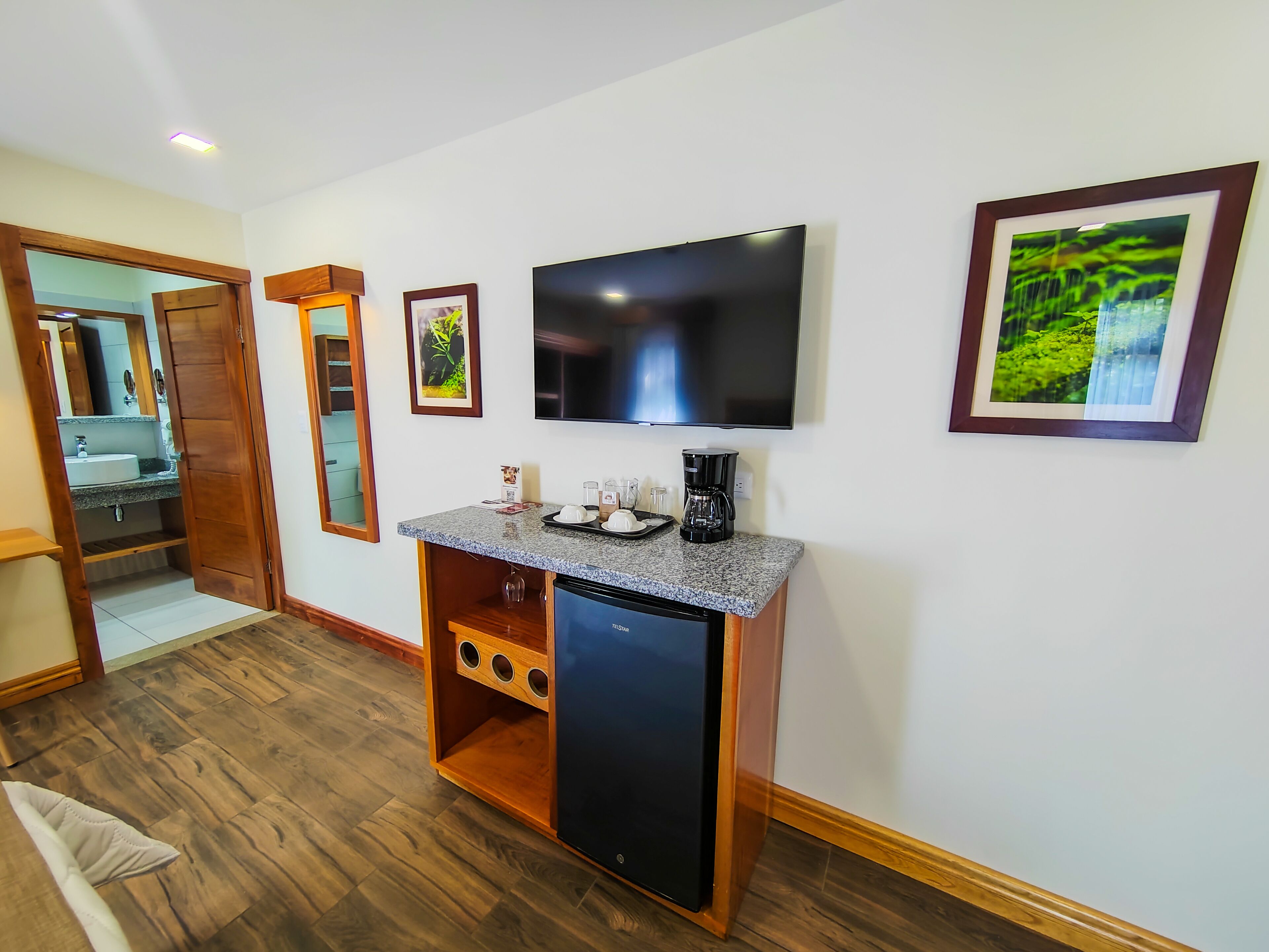 Quarto compacto com piso de madeira, televisão integrada, cafeteira e um pequeno refrigerador.