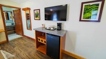 Quarto compacto com piso de madeira, televisão integrada, cafeteira e um pequeno refrigerador.