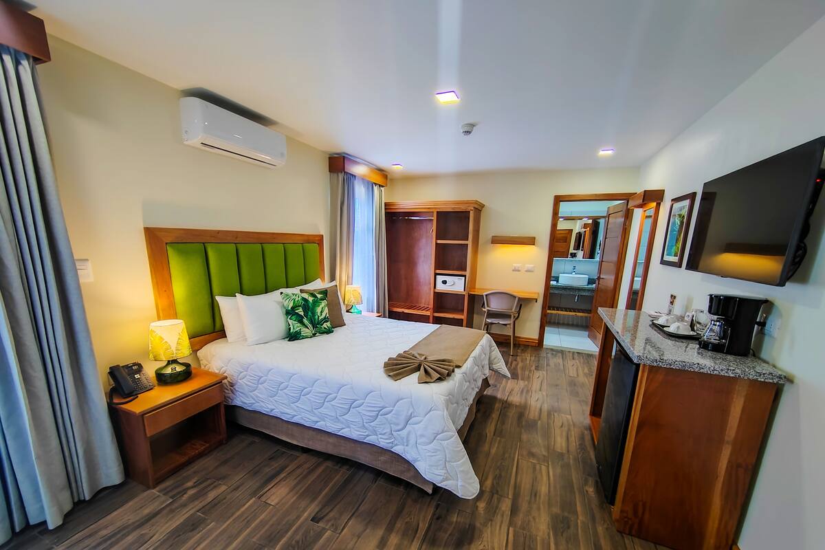 A hotel room with a bed, bedside table, lamp, and a desk with a chair.