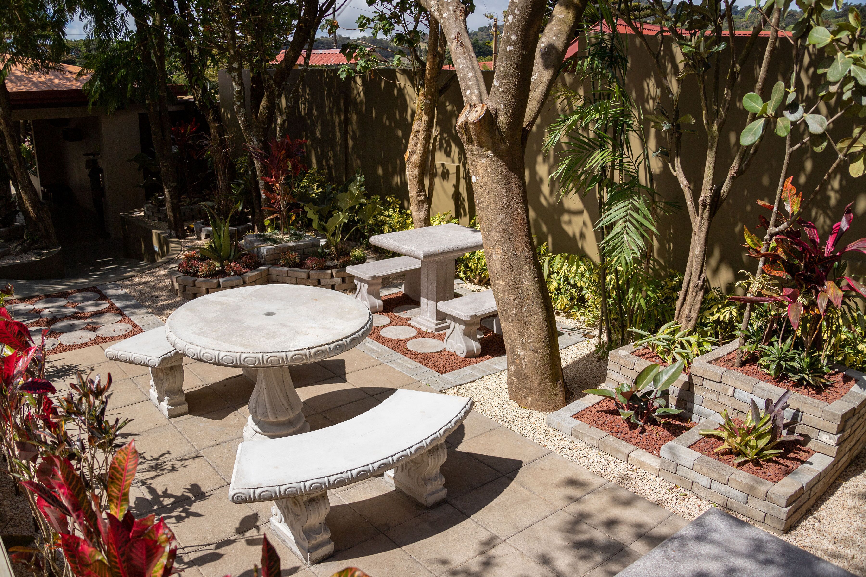 A patio with a round table and benches, surrounded by potted plants and a tree.