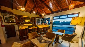 A bar area with a wooden ceiling and a view of a body of water through large windows. - Sibu Boutique Hotel (Monteverde)