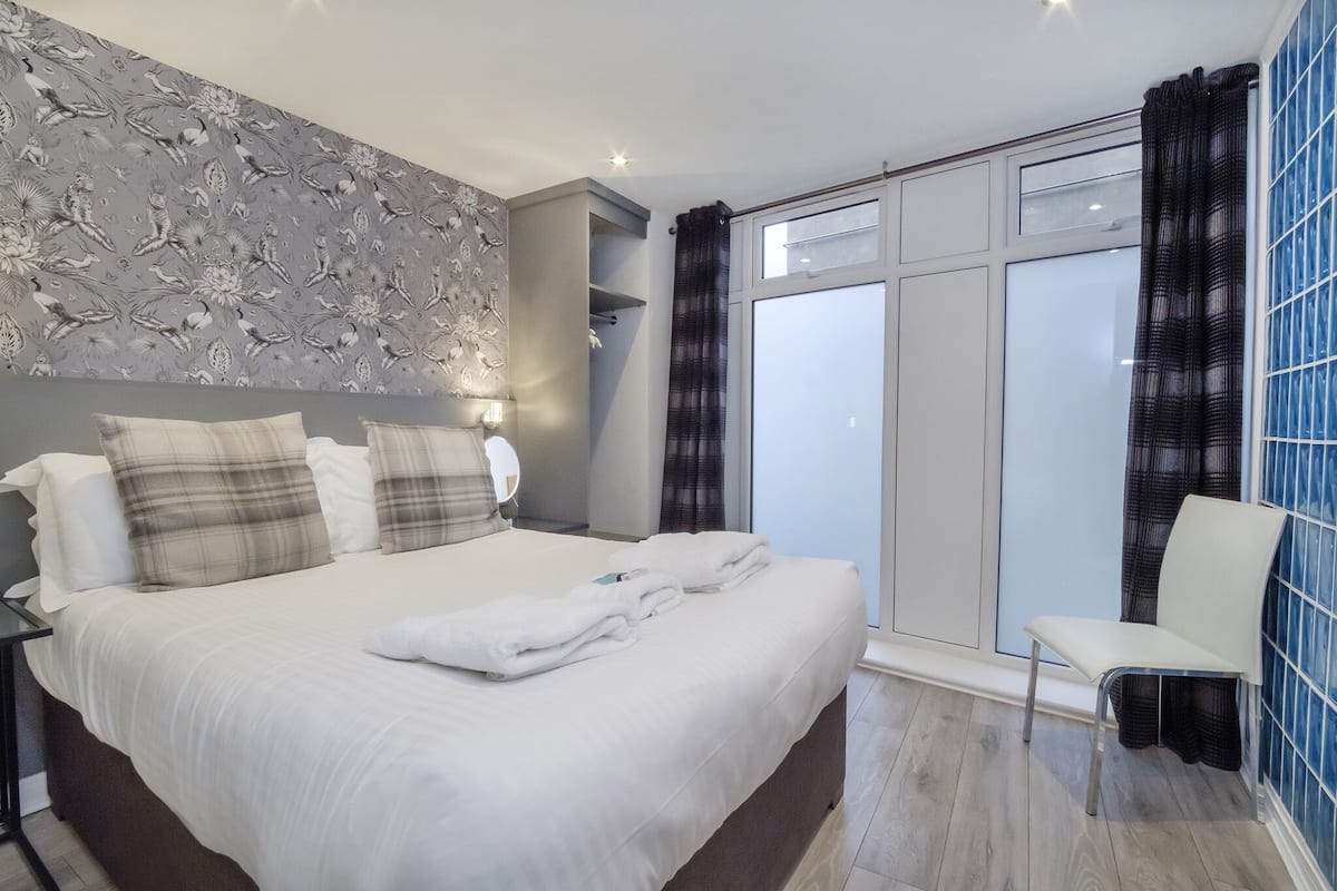 A modern hotel room with a large bed, a seating area, and a view of the outside.