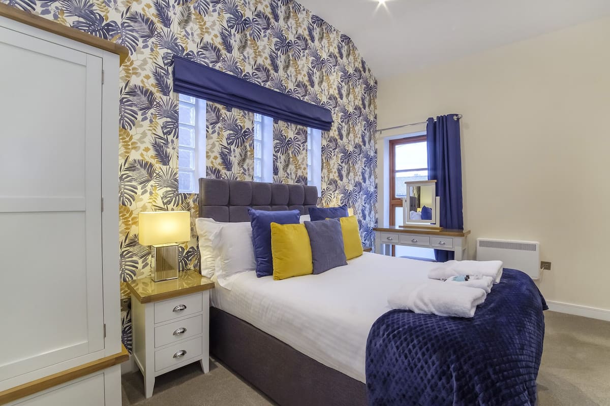 A bedroom with a bed, bedside table, lamp, and a mirror.