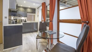 A modern kitchen with a central island, a dining area with a glass table, and orange curtains.
