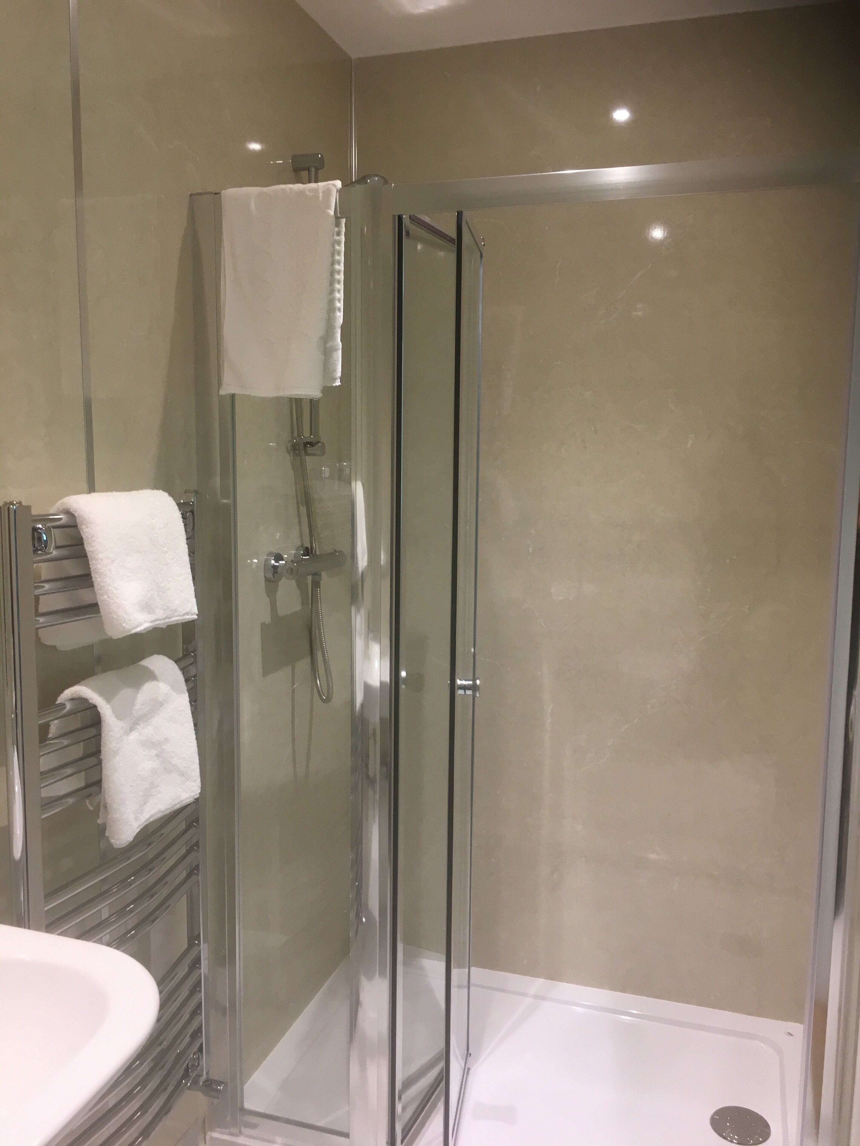 A modern bathroom with a glass-enclosed shower, a white sink, and a towel rack with multiple towels.