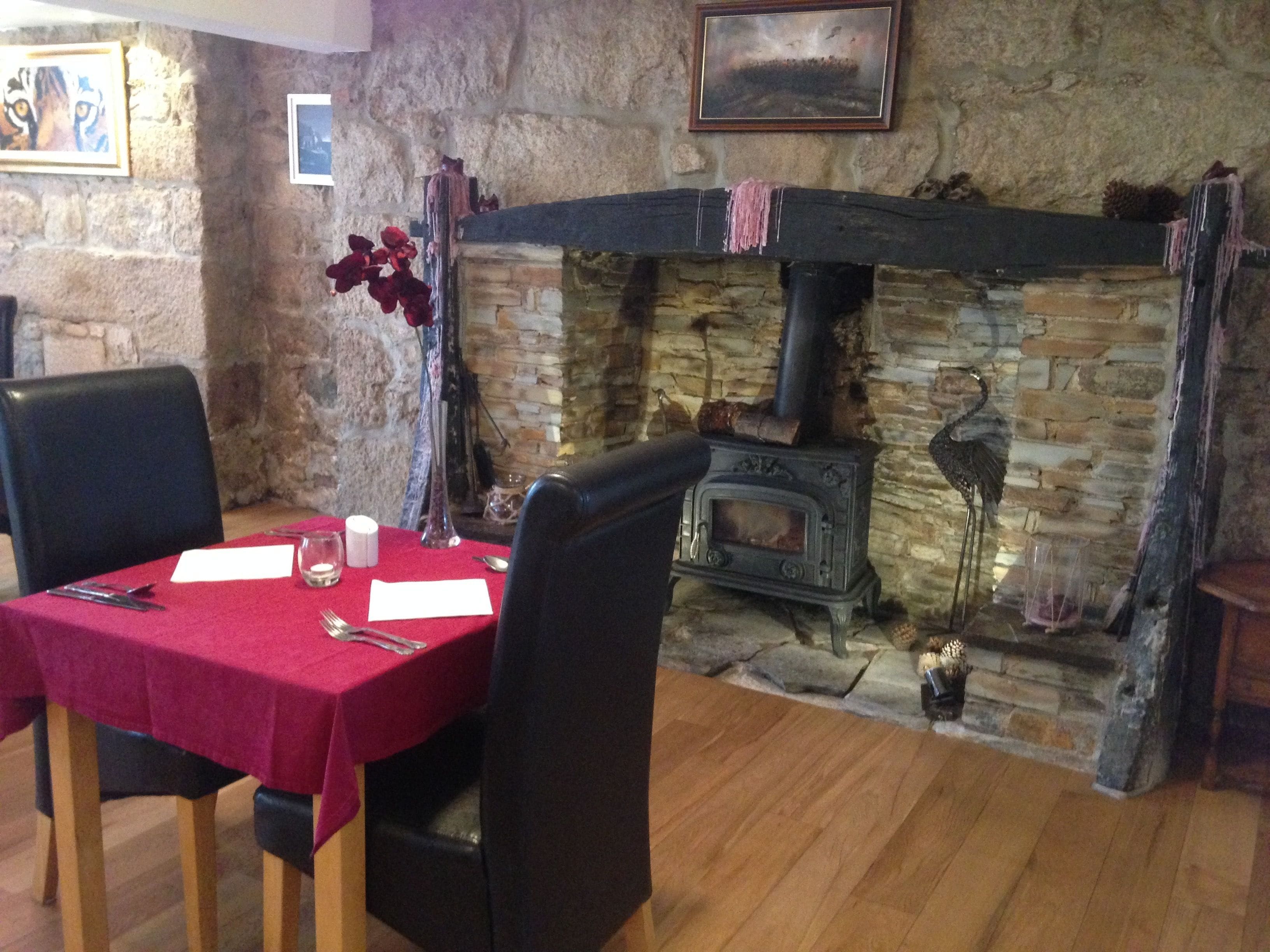 A dining area with a stone fireplace, a table set with a red tablecloth, and a wooden floor.