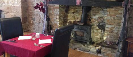 A dining area with a stone fireplace, a table set with a red tablecloth, and a wooden floor.