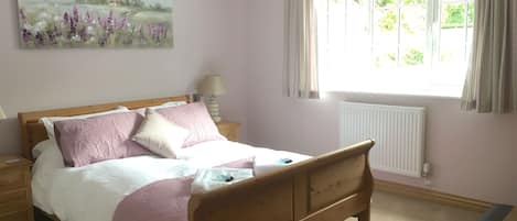 Un dormitorio con cama de madera, una mesita de noche, una lámpara, una ventana con cortinas y un cuadro en la pared.