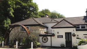 En byggnad av sten med ett stort vattenhjul, en skylt med texten ”The Waterwheel Inn” som visar att det är en restaurang och bar, och en svart hund som ligger på marken.
