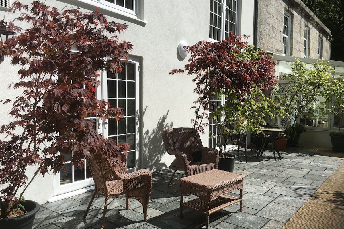 Eine Terrasse im Freien mit Korbmöbeln, Topfpflanzen und einem Gebäude mit großen Fenstern.