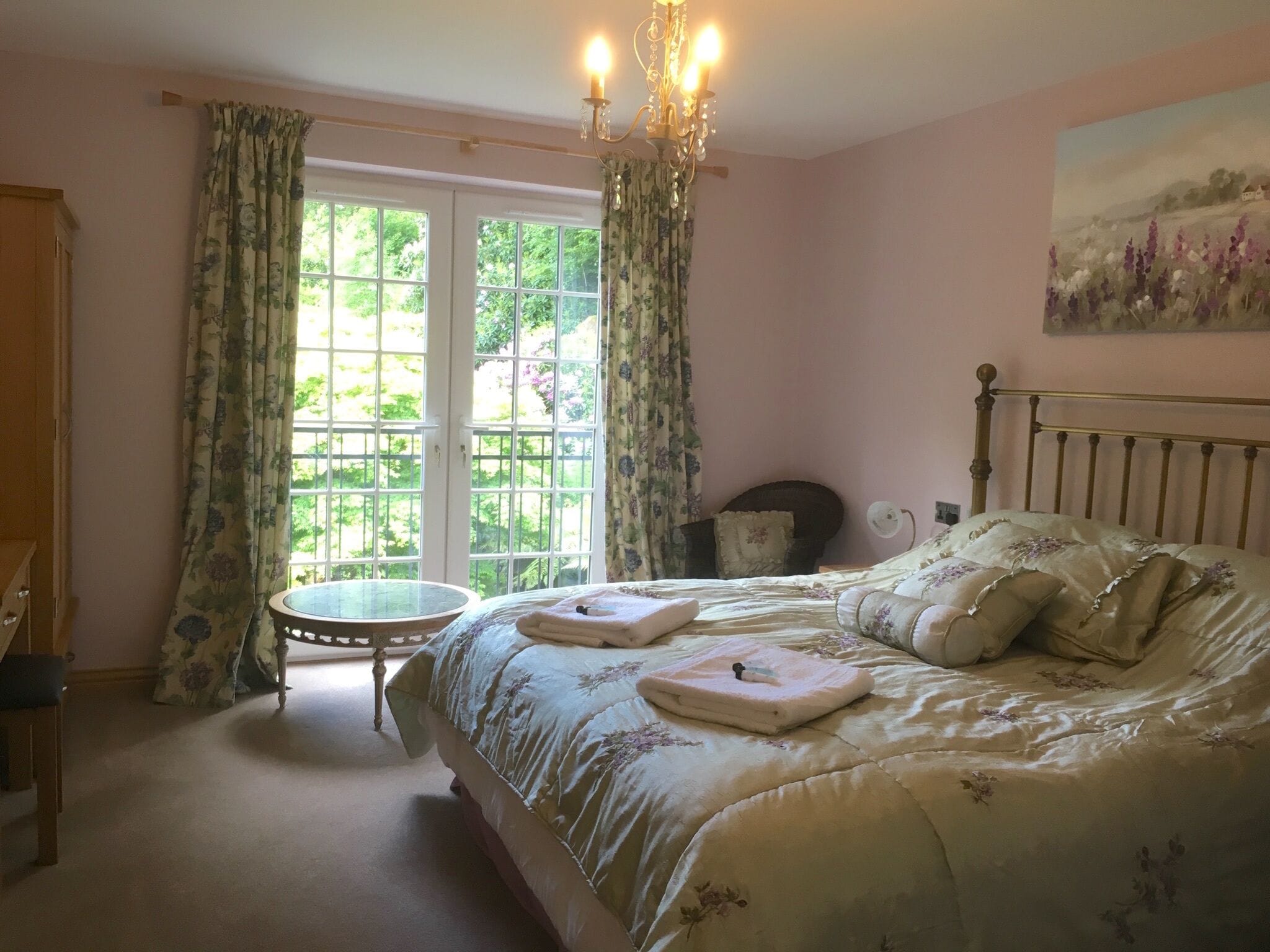 Un dormitorio con cama, una mesita redonda y una silla. Hay una ventana con cortinas y un cuadro en la pared.