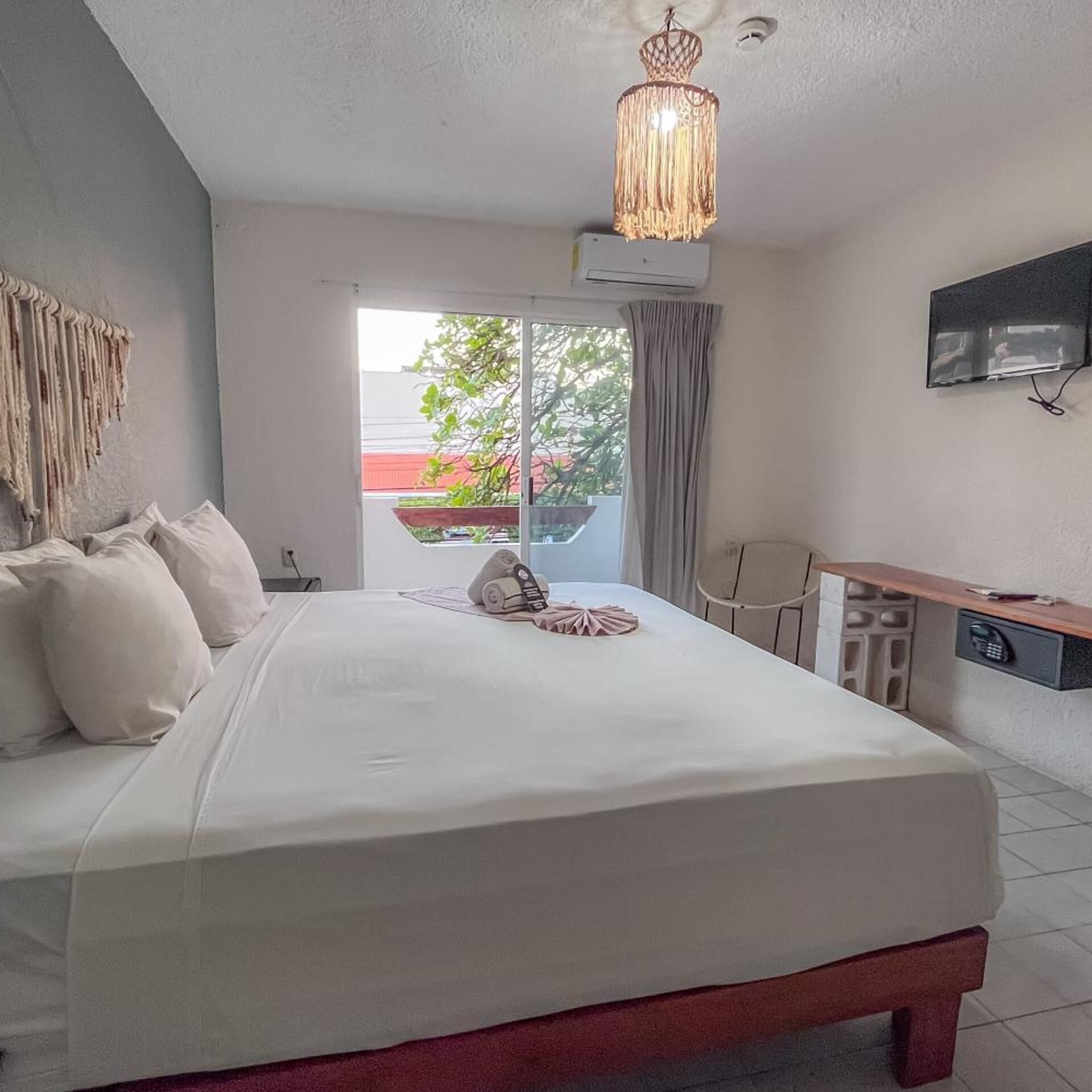 Ein Hotelzimmer mit einem großen Bett, einem Schreibtisch, einem Sessel, einem Fernseher und einem Balkon mit Blick auf Grünflächen.