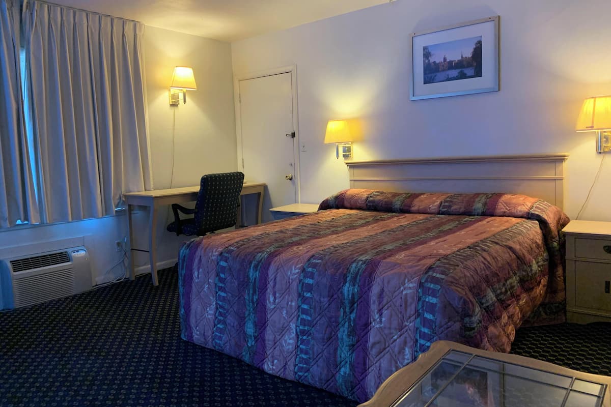 A hotel room with a bed, desk, chair, and two bedside lamps.