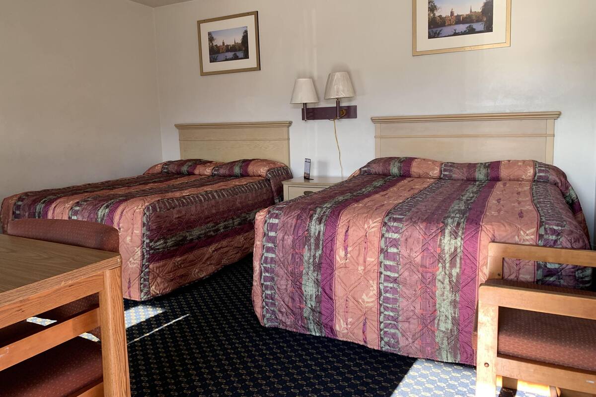A hotel room with two beds, a small table, and two lamps.