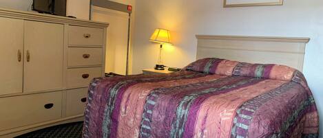 Habitación de hotel con cama, cómoda, televisor, lámpara y un cuadro en la pared.