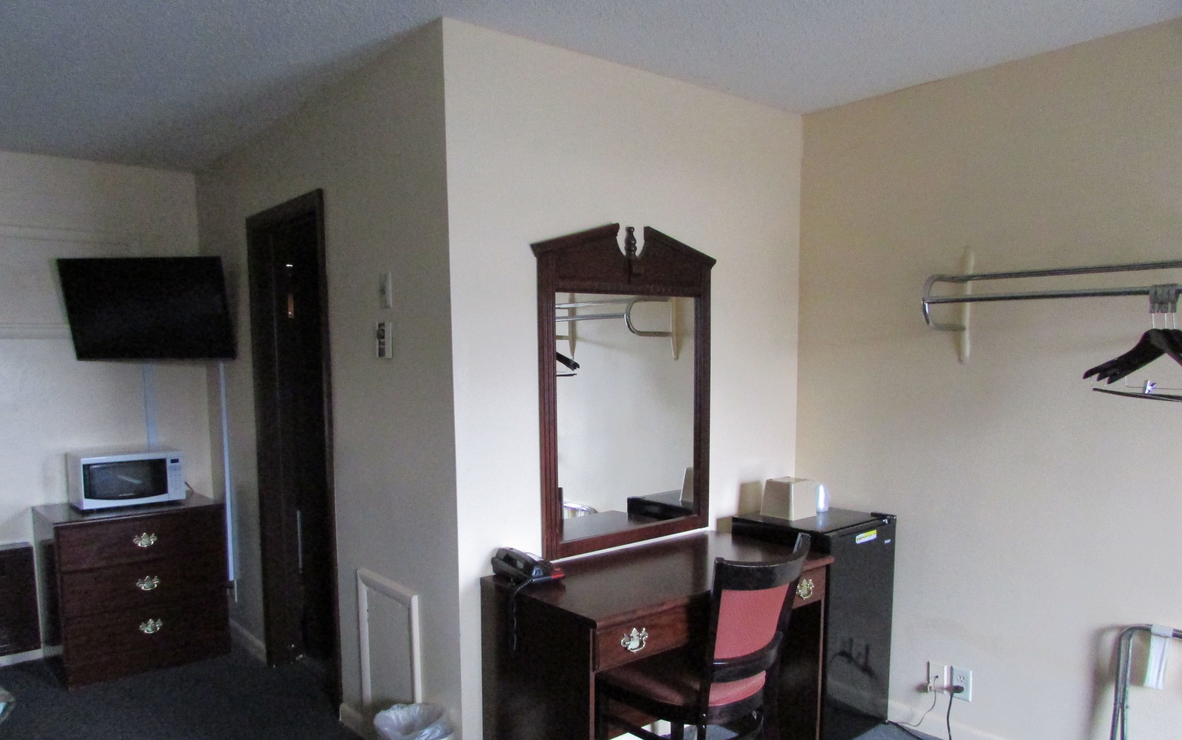 A hotel room with a wooden dresser, a mirror, a television, and a small desk with a telephone.