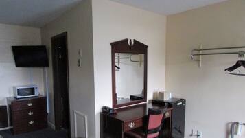 A hotel room with a wooden dresser, a mirror, a television, and a small desk with a telephone.