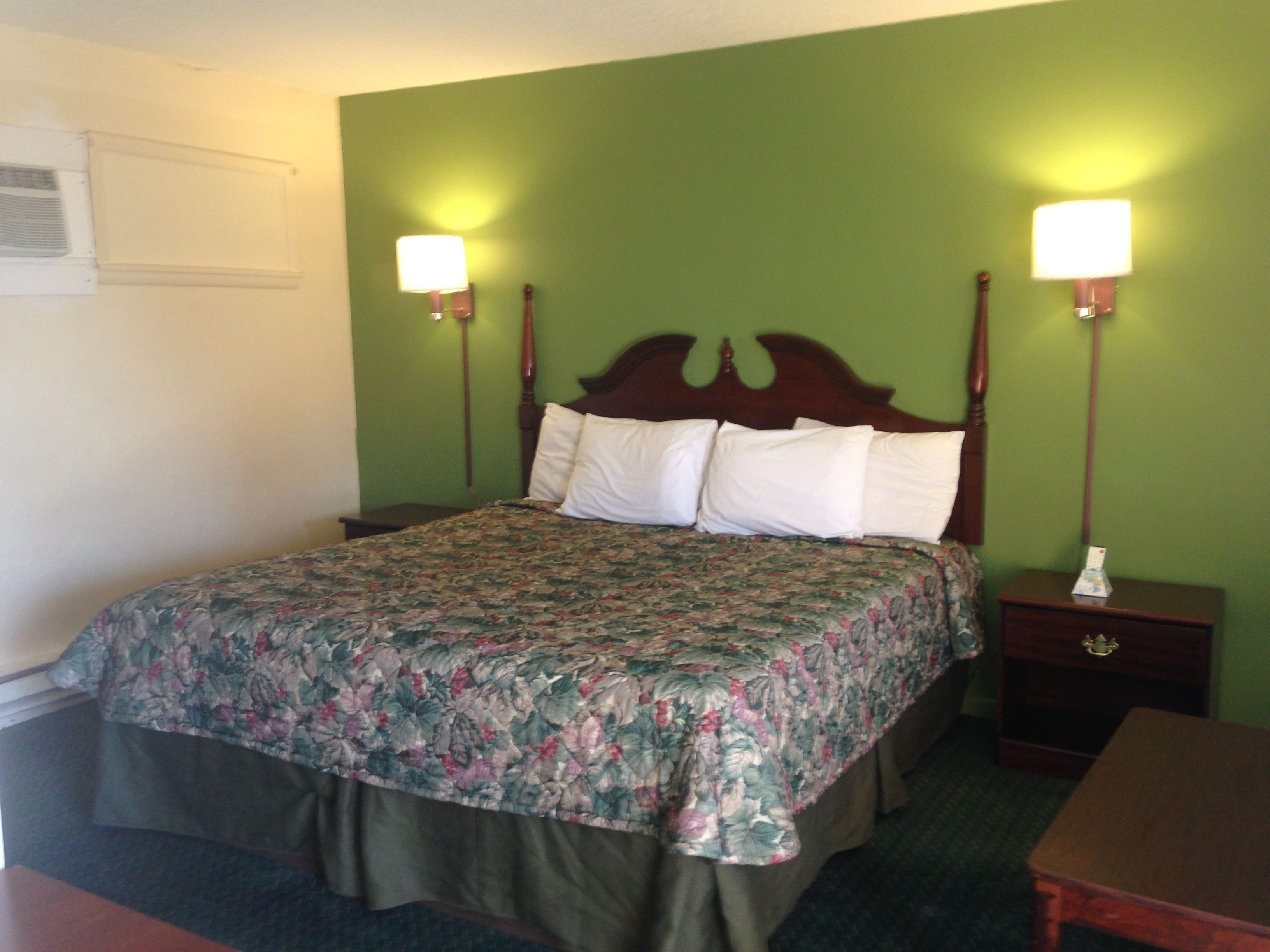 Habitación de hotel con colcha estampada, cabecera de madera, dos lámparas de noche y mesita con cajón.
