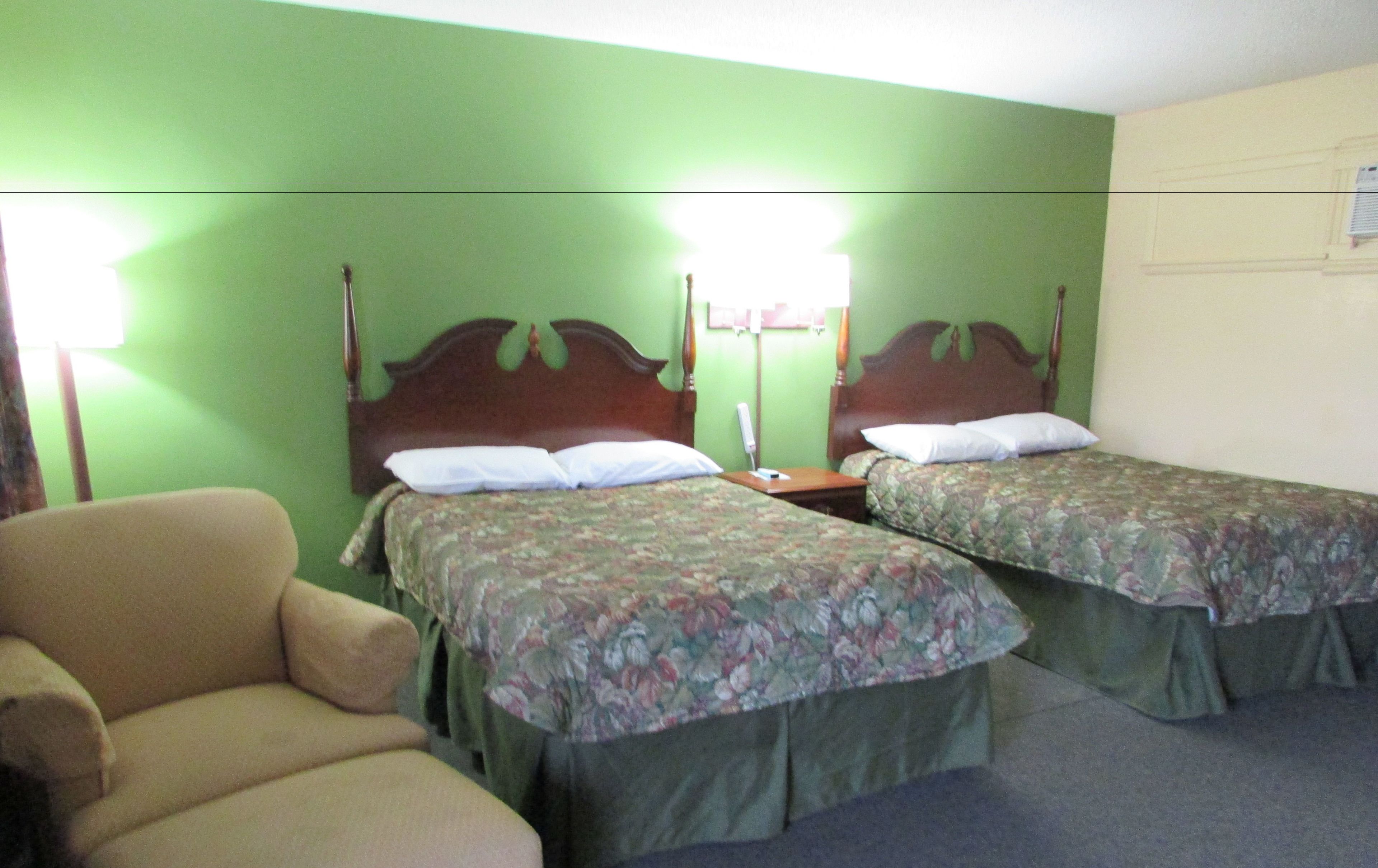 A hotel room with two single beds, a chair, and a nightstand with a lamp.