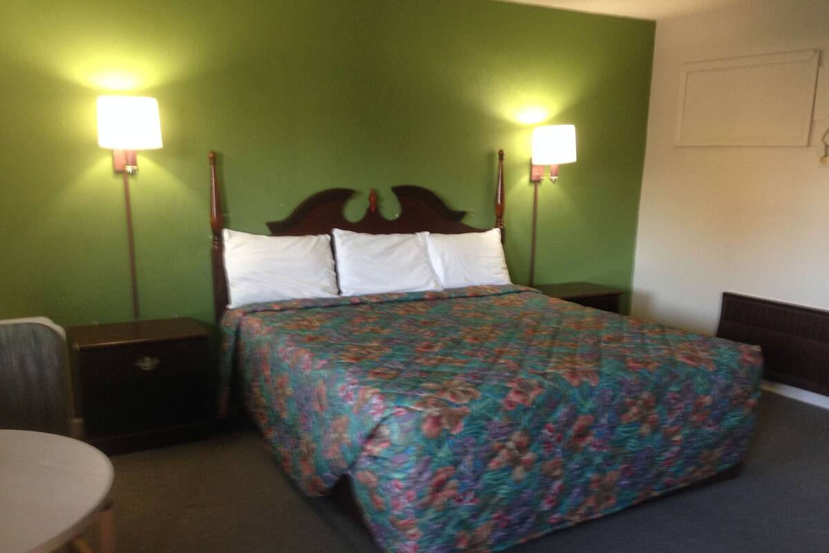 Una cama bien hecha con una colcha estampada de flores, dos lámparas de noche y un cabecero de madera.