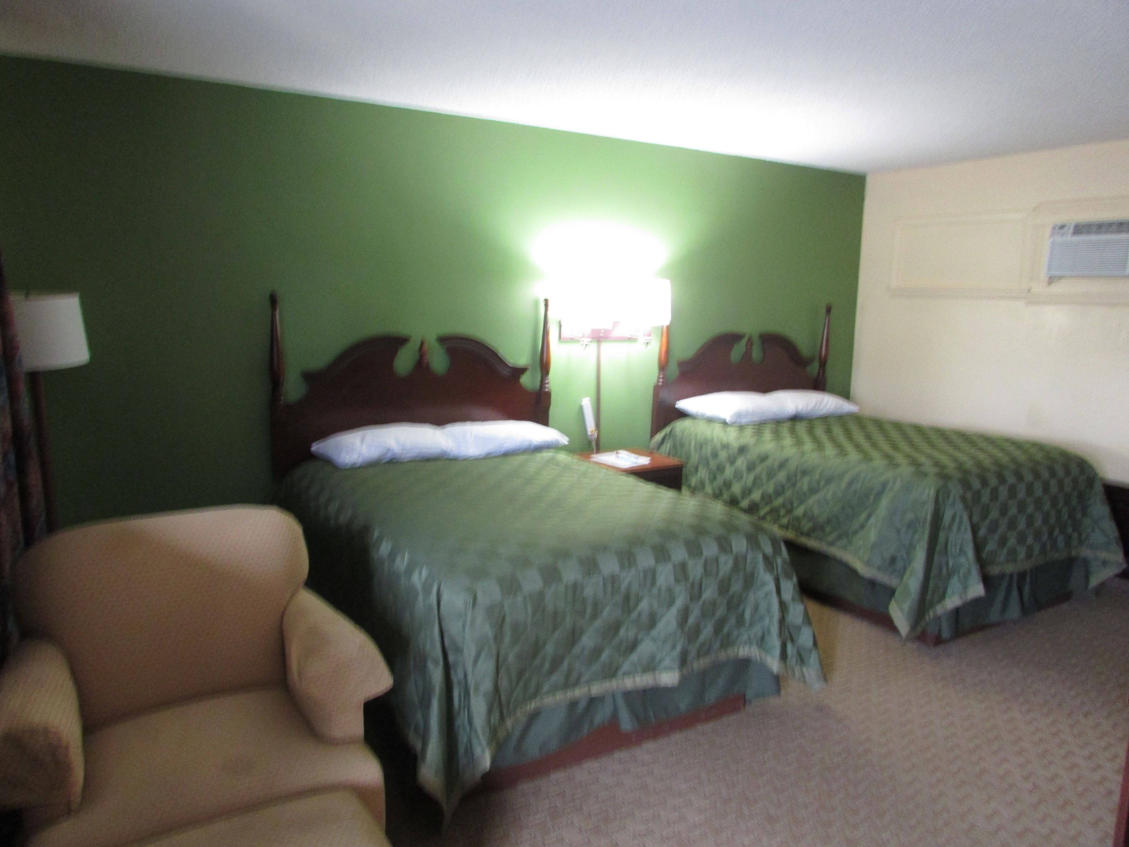 A hotel room with two single beds, a chair, and a nightstand with a lamp.