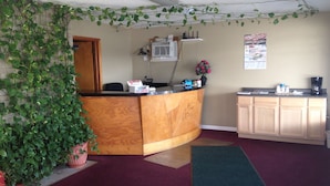 A reception area with a wooden reception desk, a potted plant, a small kitchen area with a coffee maker, and a bulletin board on the wall. - Gas Lite Motel (Lawrenceville)