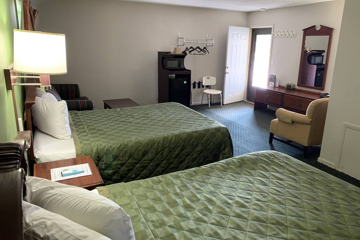 Habitación de hotel con dos camas, un escritorio, una silla, un televisor, un espejo y una puerta.