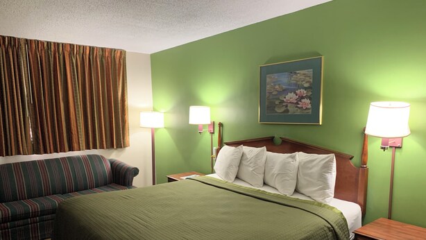 A hotel room with a bed, a sofa, two bedside lamps, a painting, and curtains. - Gas Lite Motel (Lawrenceville)