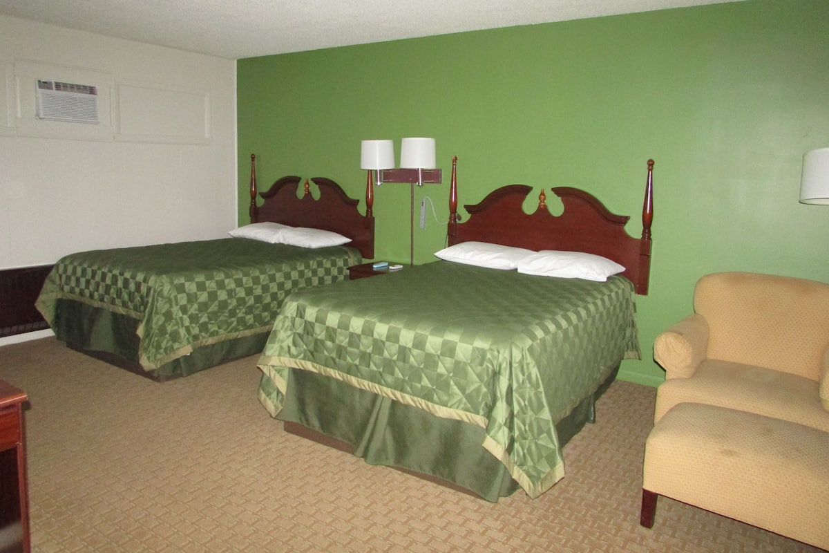 Habitación de hotel con dos camas individuales, una silla y una mesita de noche con lámparas.