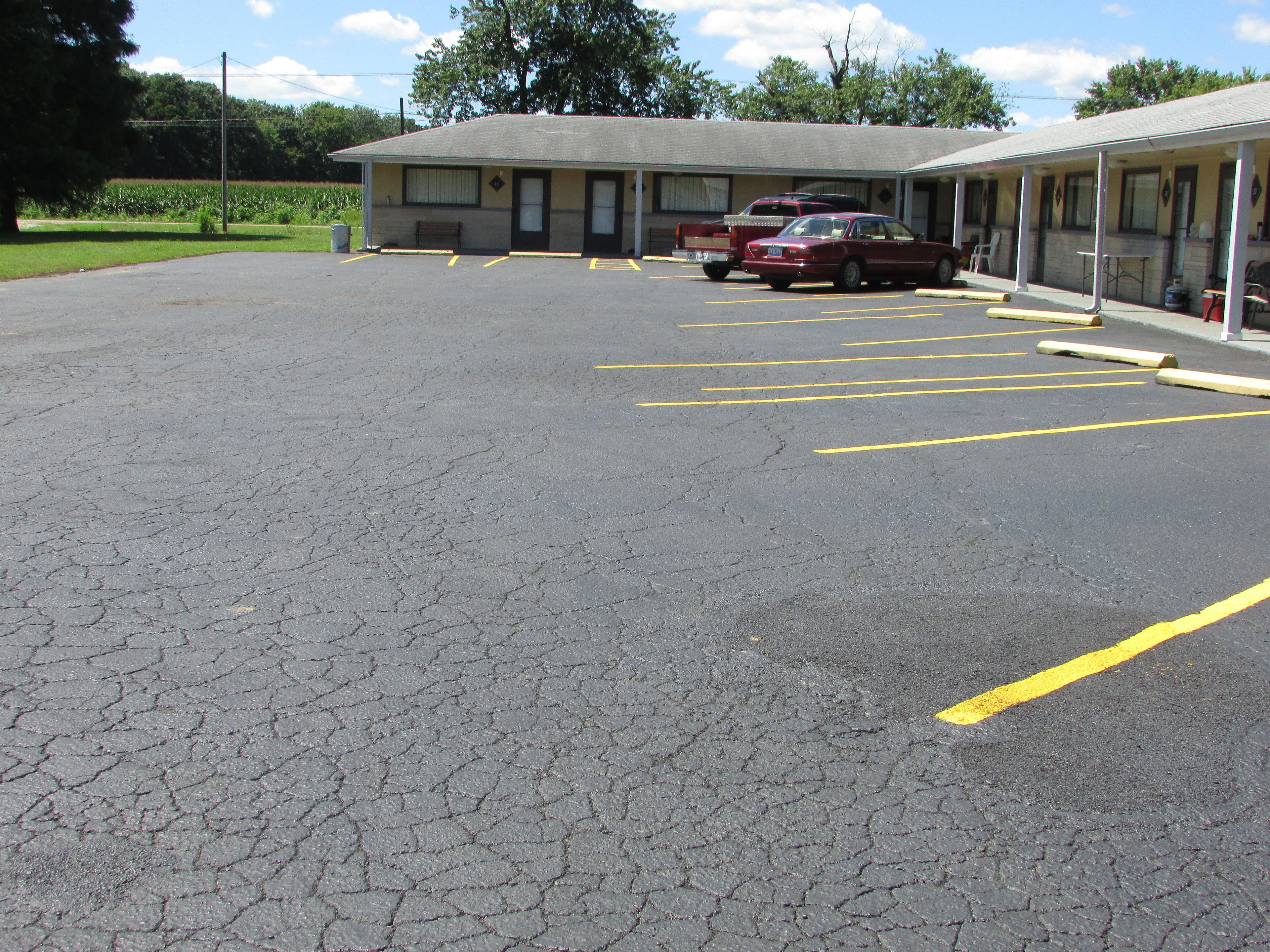 A parking lot with multiple marked parking spaces, a building with a flat roof, and a row of parked cars.
