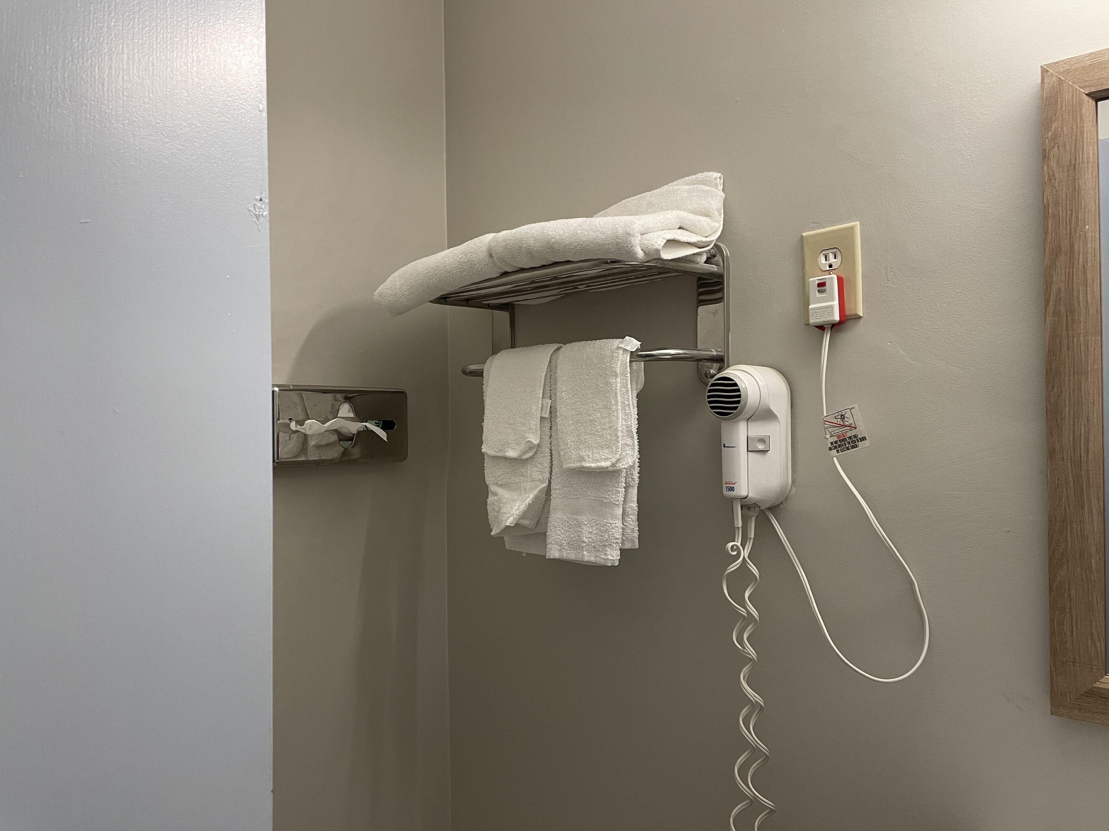 A bathroom with a towel rack holding two towels, a hairdryer, and a small photo frame on the wall.