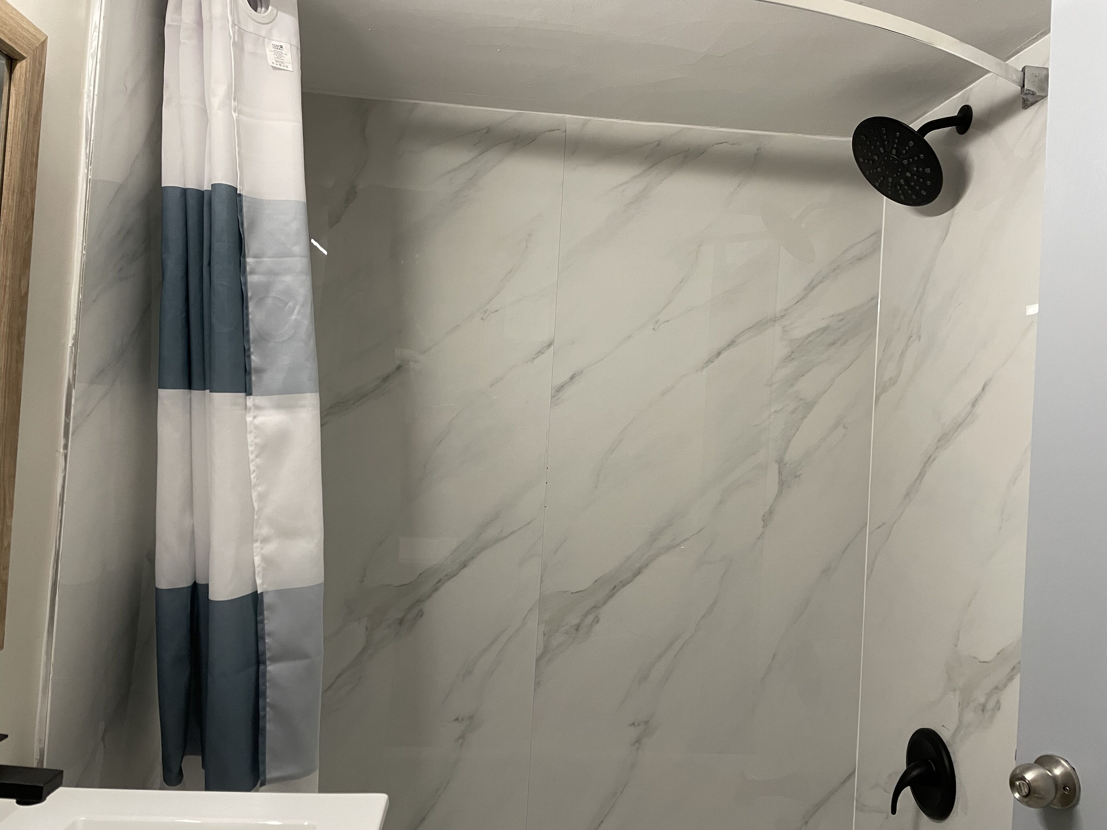 A bathroom with a shower, a curtain, and a door with a handle.