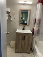Un baño con un mueble de madera, un lavamanos blanco, un secador de pelo y un espejo.