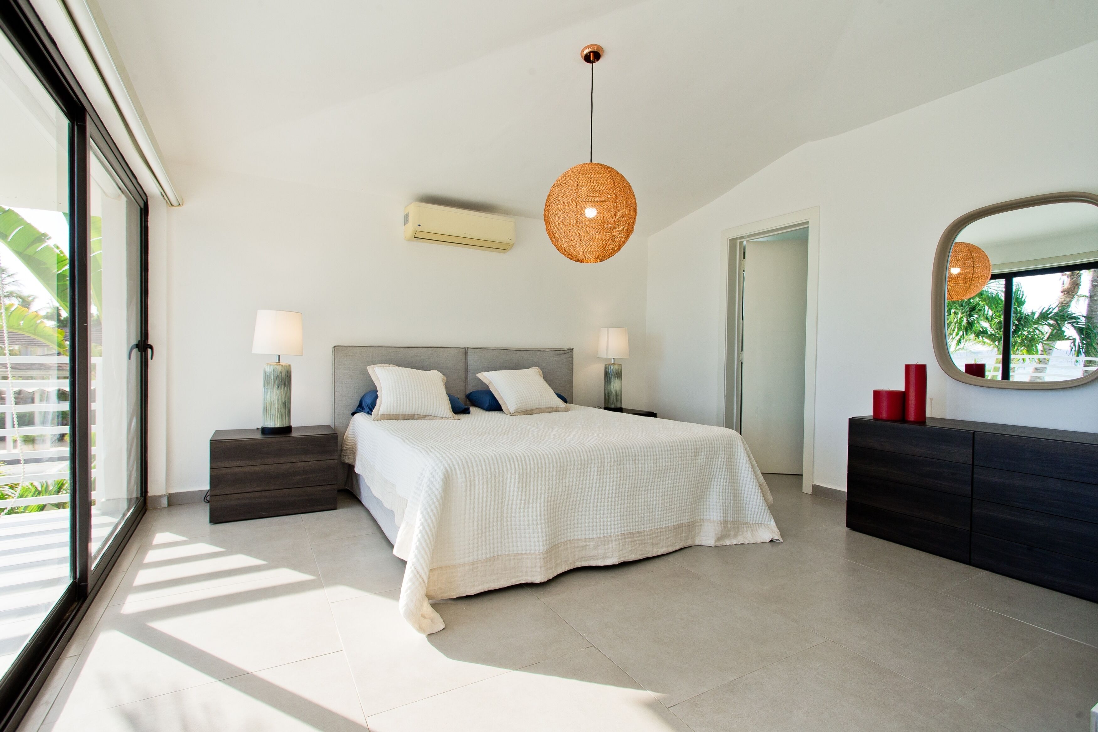 A modern bedroom with a large bed, bedside lamps, a hanging light fixture, a mirror, and a dresser.